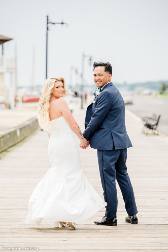 bride and groom pose on the boardwalk by the ocean
